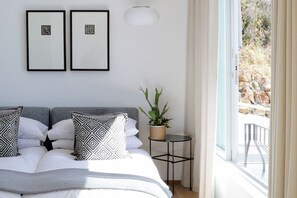 A bedroom with a bed, two framed pictures, a potted plant, and a view of a balcony.