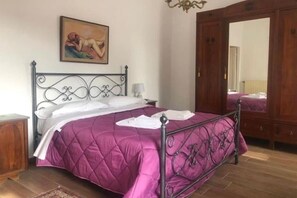 A bedroom with a bed, a wooden wardrobe, a mirror, and a painting on the wall.
