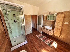 A modern bathroom with a glass shower enclosure, a wooden vanity with a sink, and a patterned rug on the floor.