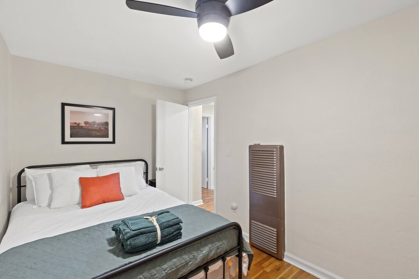A bedroom with a bed, a bedside table, a heater, and a ceiling fan.