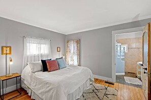 Un dormitorio con cama, mesitas de noche, lámpara y vistas al baño.
