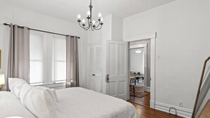 Une chambre à coucher avec un grand lit, un lustre, une armoire et une porte donnant sur un coin repas.