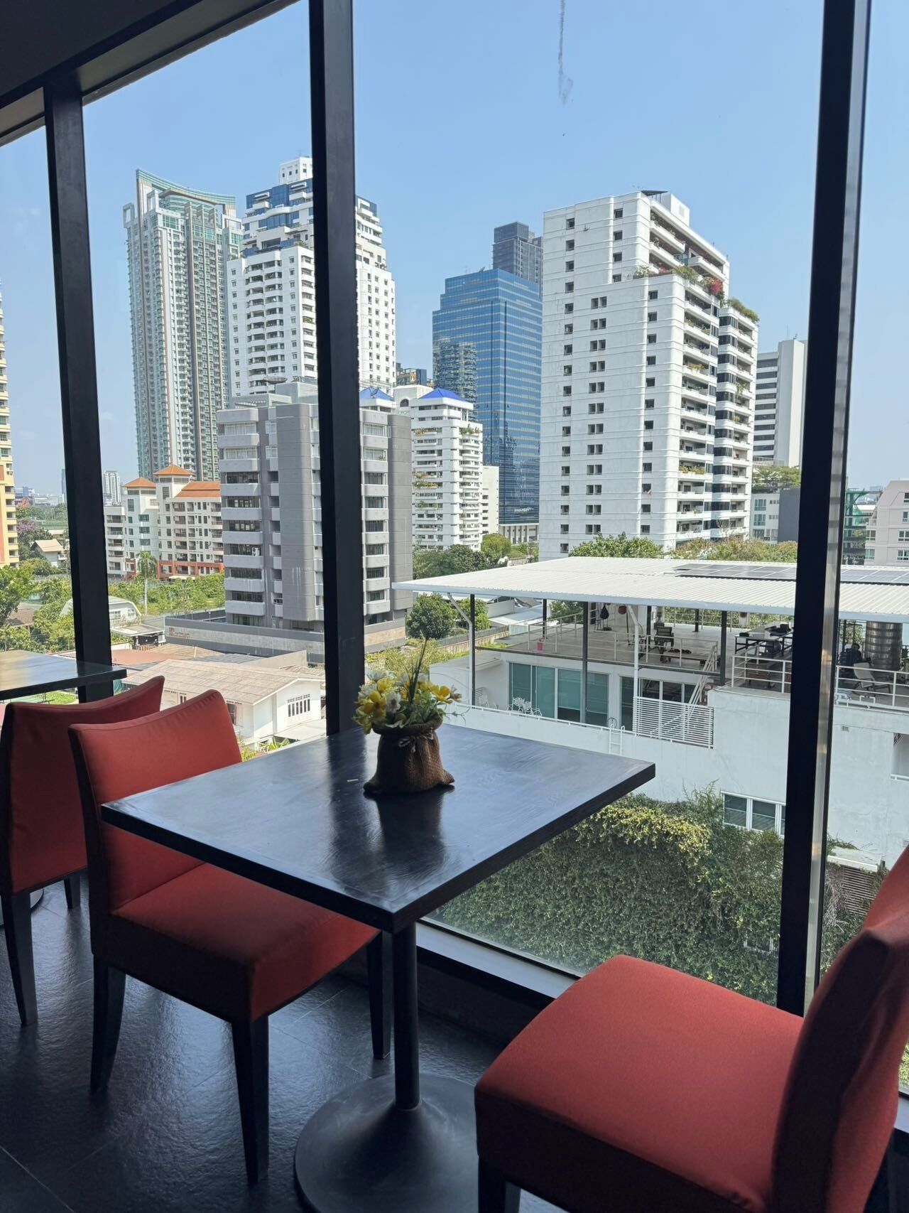 Un comedor moderno con una mesa y sillas rojas, ventanas amplias que ofrecen vistas a la ciudad y una planta pequeña sobre la mesa.