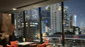 Un restaurant moderne avec des chaises et des tables rouges, de grandes fenêtres offrant une vue sur la ville la nuit.
