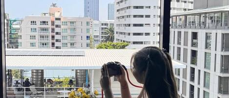 A person sitting by a window with a camera, overlooking a cityscape with modern buildings.