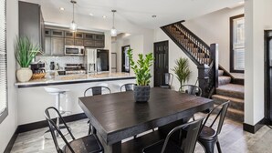 A modern kitchen with a central island, stainless steel appliances, and a dark wood dining table with chairs. - Stylish 4BR Home • Close to Hospitals + Downtown (Cleveland)