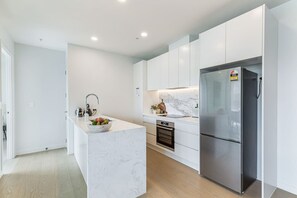 A modern kitchen with white cabinetry, a marble countertop, a stainless steel refrigerator, and a built-in oven. - Brand New! Luxe 3BR In Aotea Square I Zodiak Stays (Auckland)