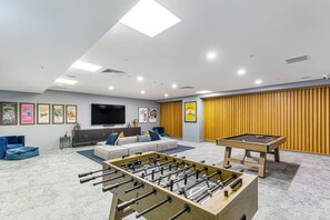 A modern living room with a foosball table, a pool table, a sofa set, a flat-screen TV, and a wall with framed movie posters. - Brand New! Luxe 3BR In Aotea Square I Zodiak Stays (Auckland)