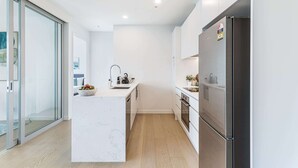 Une cuisine moderne dotée d’un îlot en marbre, d’appareils électroménagers en acier inoxydable et d’une porte en verre donnant sur un balcon.