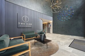 Uma área de recepção com design moderno, incluindo um balcão de atendimento, espaço de estar com sofás verdes, uma parede decorativa com um logotipo e uma instalação artística original.