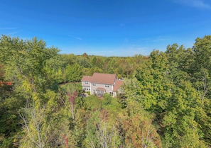 A two-story house surrounded by dense forest. - Fireside Retreat | Wooded Lot | Center Fireplace | Patio | Fire Table | Grill (South Haven)