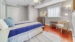 Une chambre à coucher comprenant un lit, une chaise, une commode, un ventilateur de plafond et une fenêtre avec des stores.