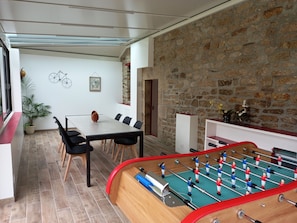 Une pièce avec une table de baby-foot, une table à manger avec des chaises, une plante en pot et un mur en pierre.