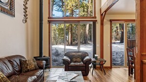 A spacious living room with a leather sofa, a coffee table, and a large window offering a view of trees. - Golfers View - on Golf Course - Close to park and lake (McCall)