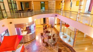 En hotellobby i flere etager med en buet trappe, siddeområder og en dekorativ lysekrone.