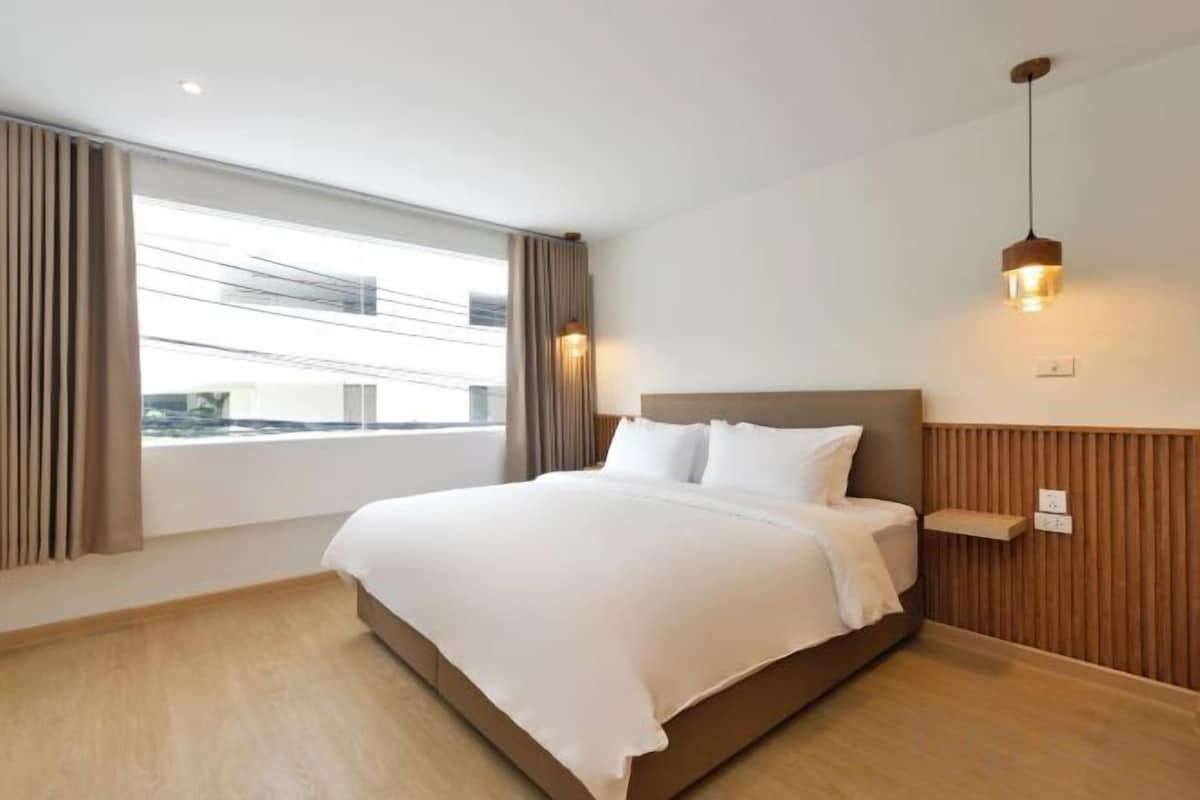 A hotel room with a bed, window, and wall-mounted light fixture.