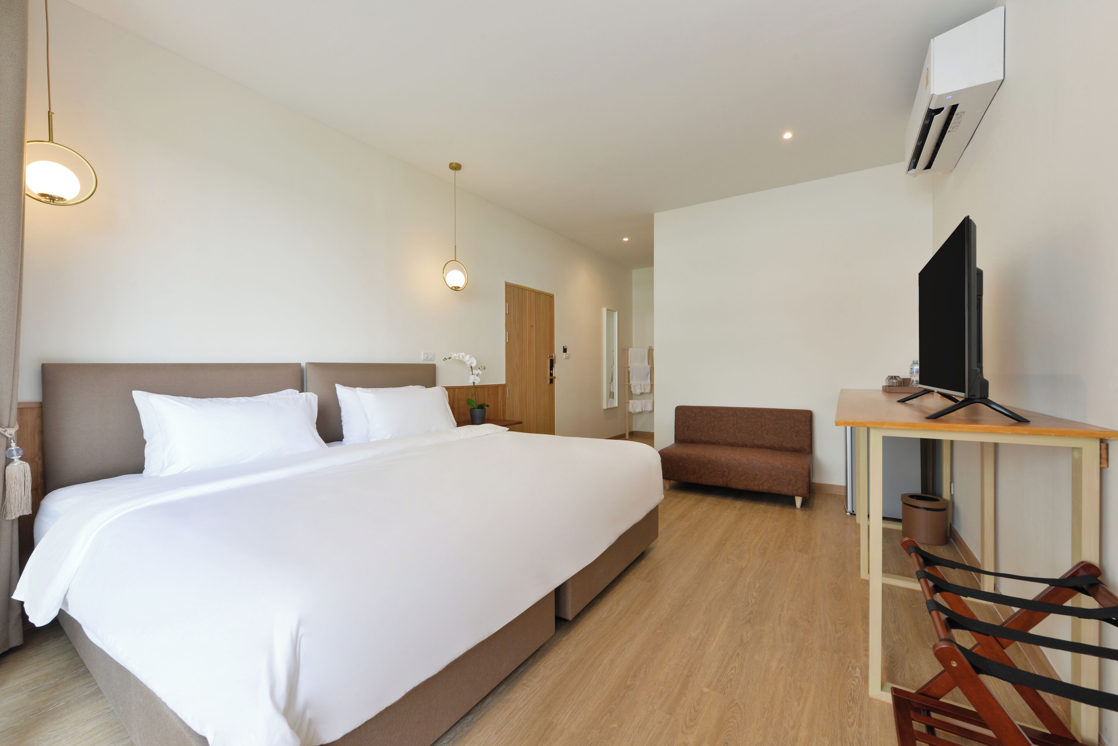 A modern hotel room with a large bed, a desk with a chair, a television, and a small trash bin.