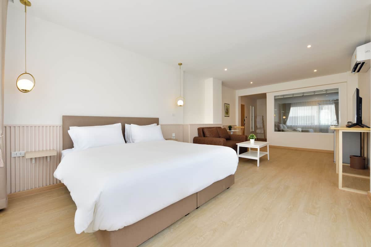 A modern hotel room with a large bed, a small sofa, a white coffee table, and a window with a view.