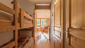 Ein Holzinnenraum mit Stockbetten, einer Holztür und Blick auf einen Außenbereich mit einer Bank und einem Tisch.