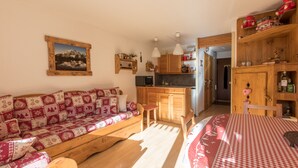 Ein gemütliches Zimmer mit einer Holzsofa, einem Esstisch mit kariertem Tischläufer, einer Küchenzeile und einer Holzkabine mit Dekorationen.