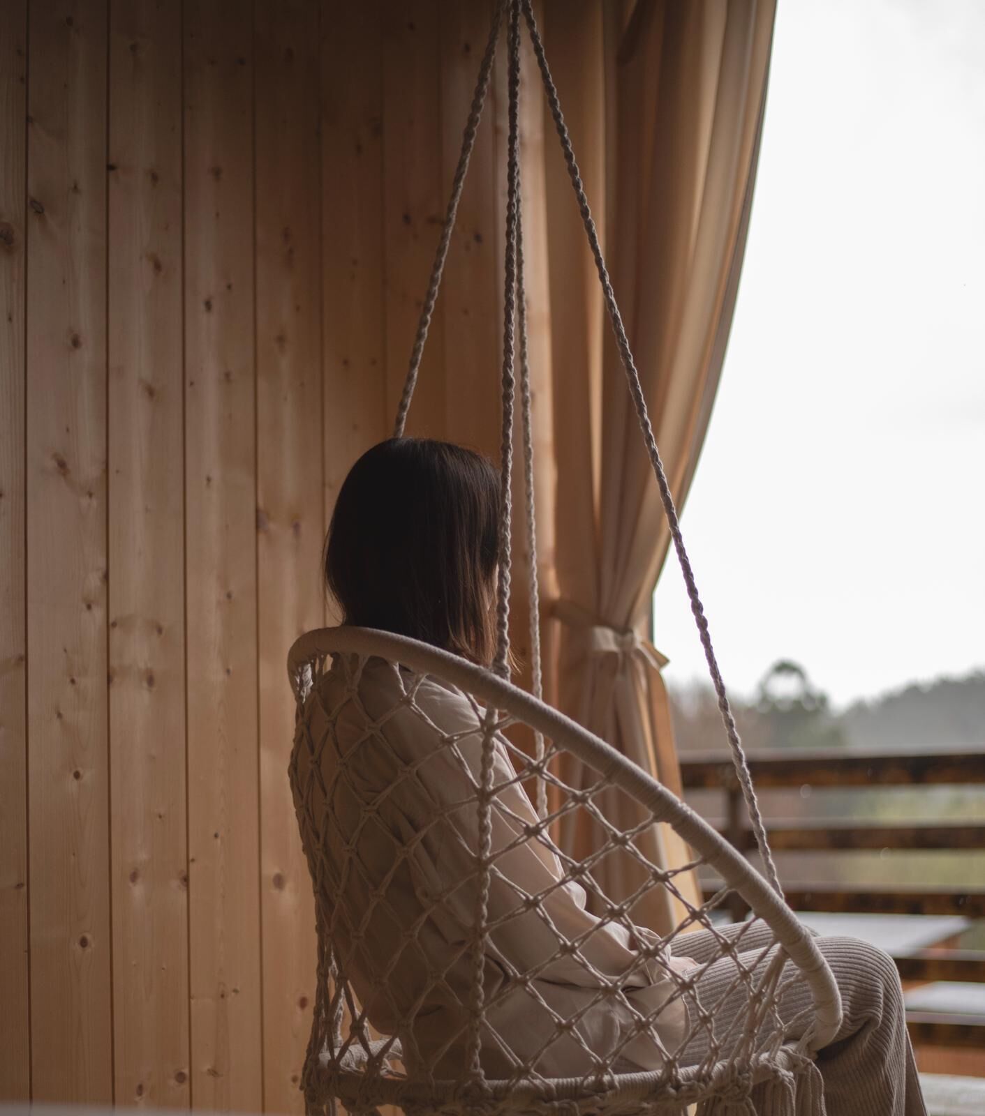 Une personne assise sur un fauteuil suspendu en macramé.