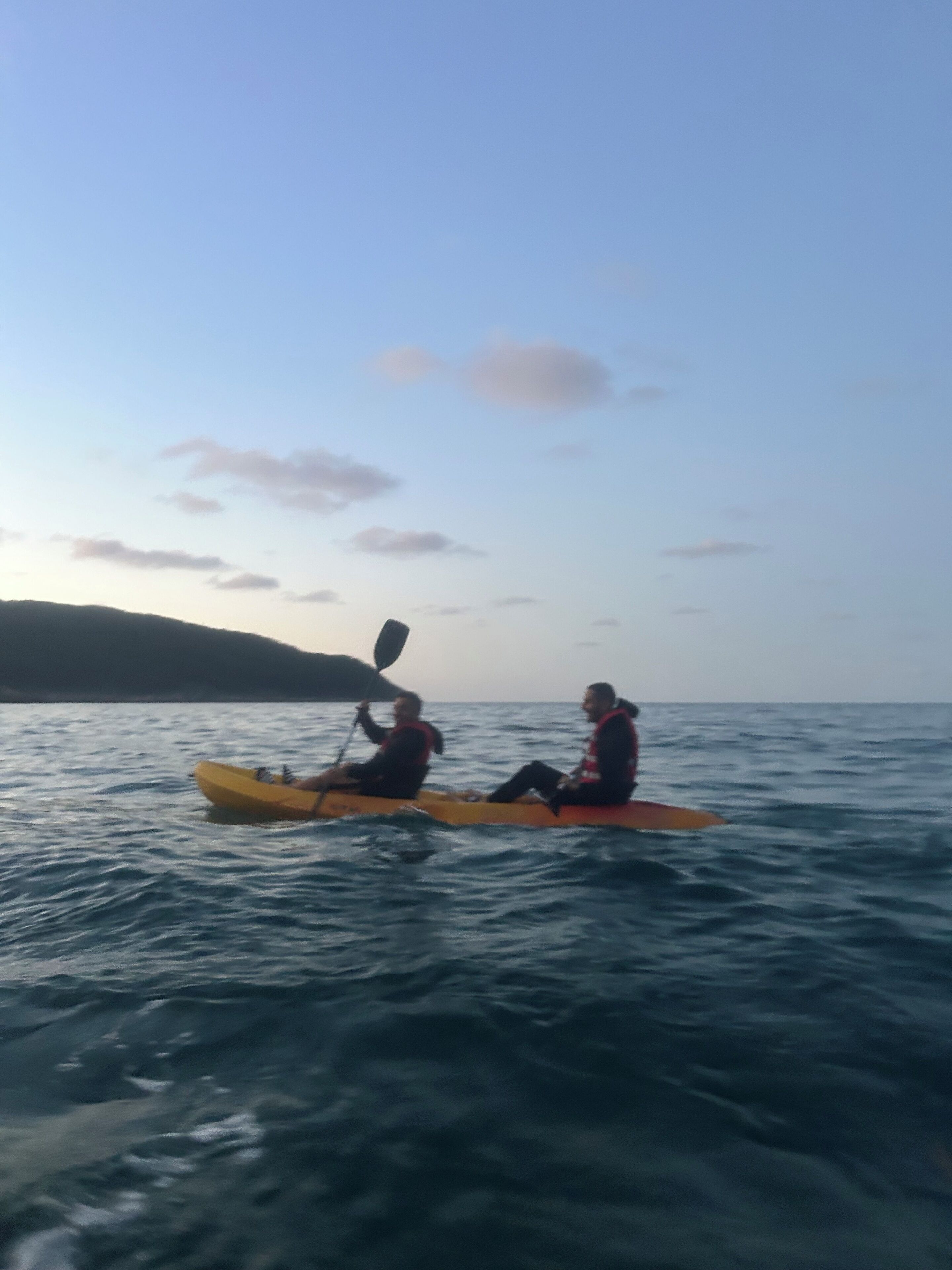 Two people kayaking on a calm sea with a clear sky.
