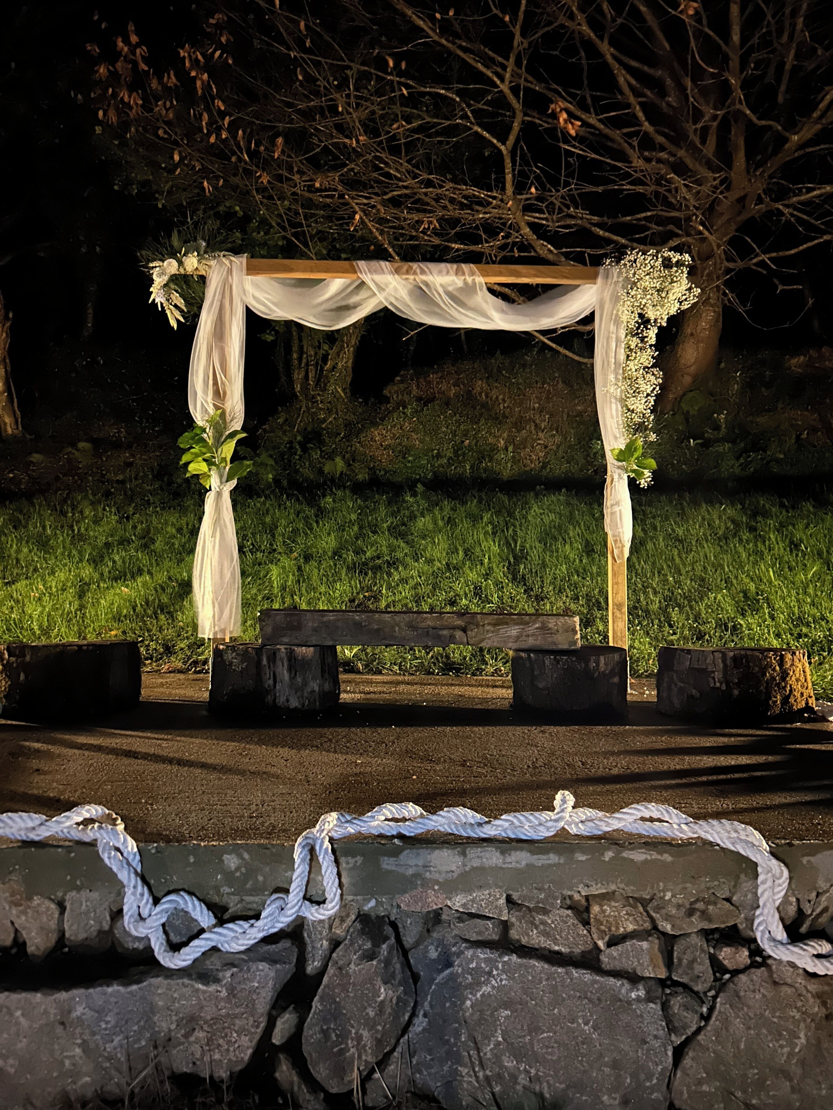 Un banco de madera con un dosel blanco cubierto y decoraciones florales en un entorno al aire libre.