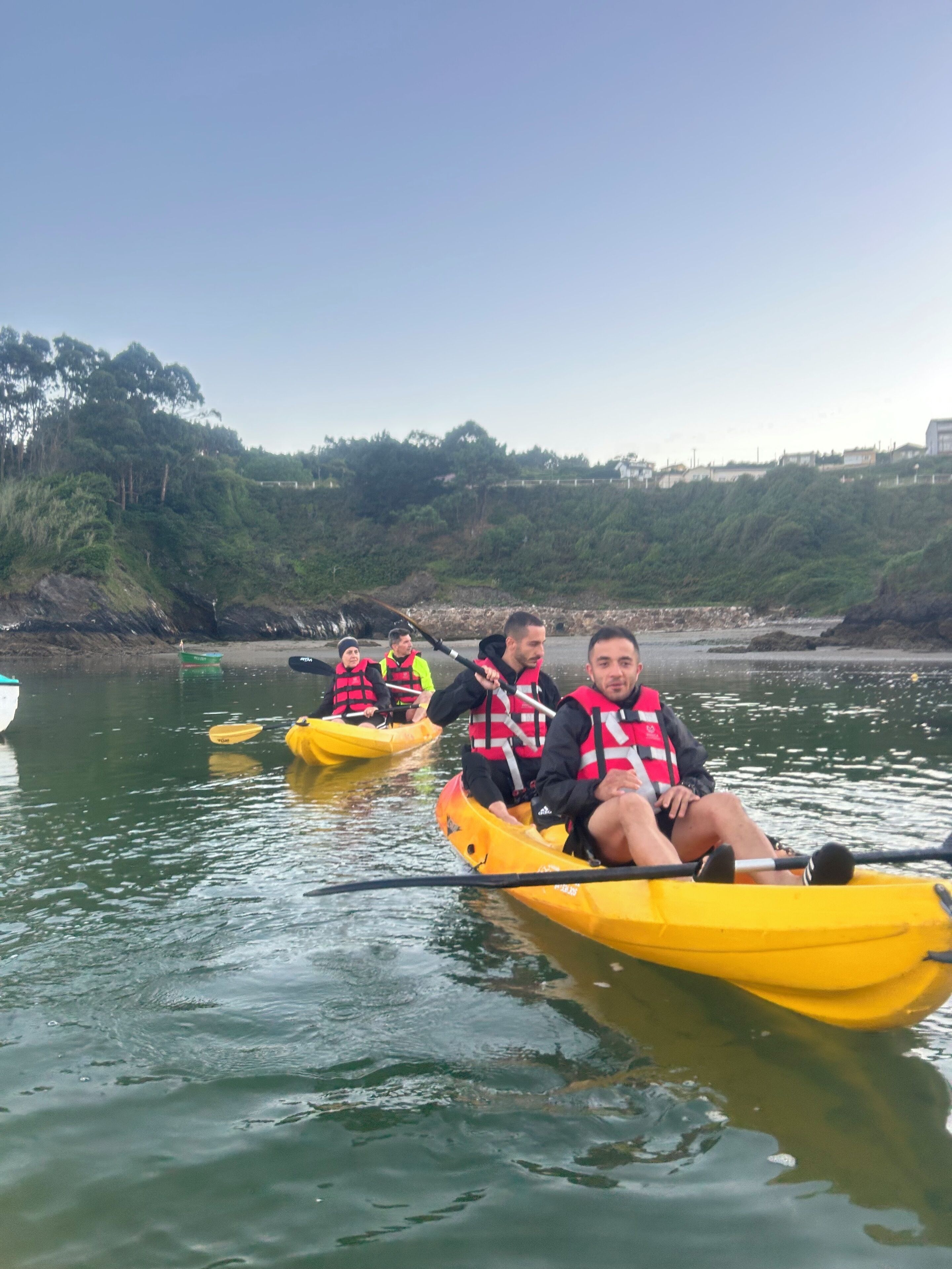 Trois personnes en kayaks jaunes sur une étendue d’eau calme, portant des gilets de sauvetage.