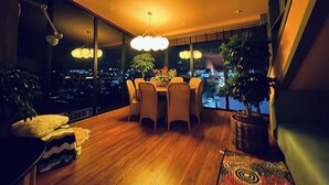 A dining area with a table and chairs, large windows, and a view of the city at night. - 9 Inn - Staycation in Am Am Dalat (Xuan Huong - Da Lat)
