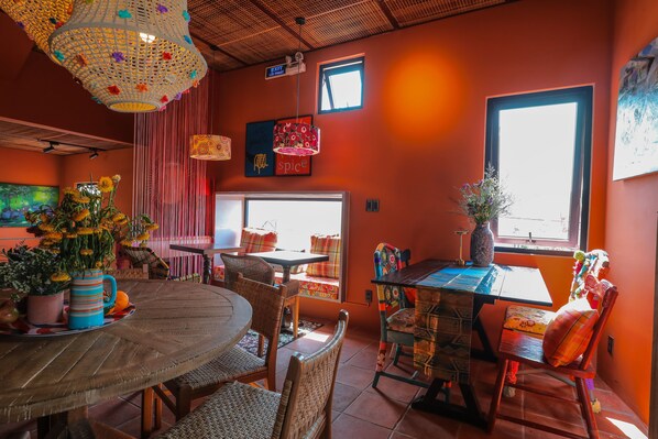 Un comedor con una mesa redonda de madera, sillas de mimbre y una lámpara colgante de colores.