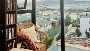 A room with a large window, a bookshelf, a wicker chair, and a lamp. - 9 Inn - Staycation in Am Am Dalat (Xuan Huong - Da Lat)
