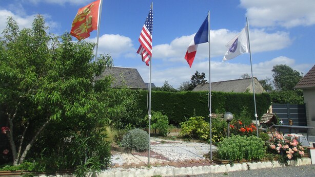 A garden with a paved walkway, surrounded by greenery and flowering plants. - Gîte le Lilas (vierville sur mer  France)