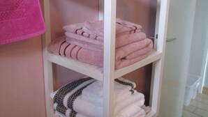 A white metal shelf unit with folded towels in various colors and patterns. - Gîte le Lilas (vierville sur mer  France)