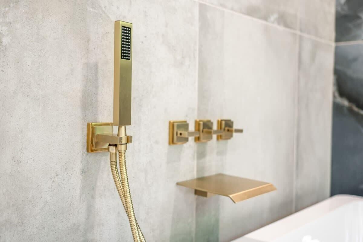 Un bagno moderno con soffione e comandi dorati, zona doccia con pareti in vetro e rivestimento in marmo.