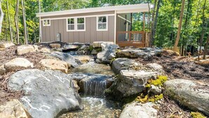 Une cabane avec une petite cascade, entourée de rochers et d’arbres.