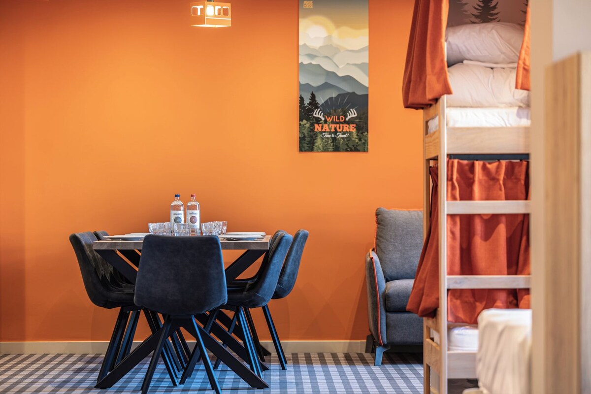 A room with a dining table set for two, a bunk bed with orange curtains, and a poster of wild nature on the wall.