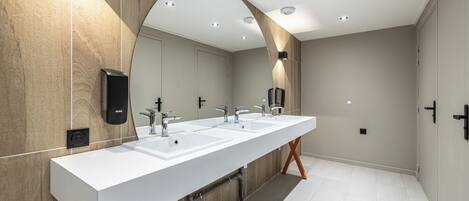 Un baño moderno con un lavabo blanco alargado, dos lavabos, un espejo grande y paneles de madera en las paredes.