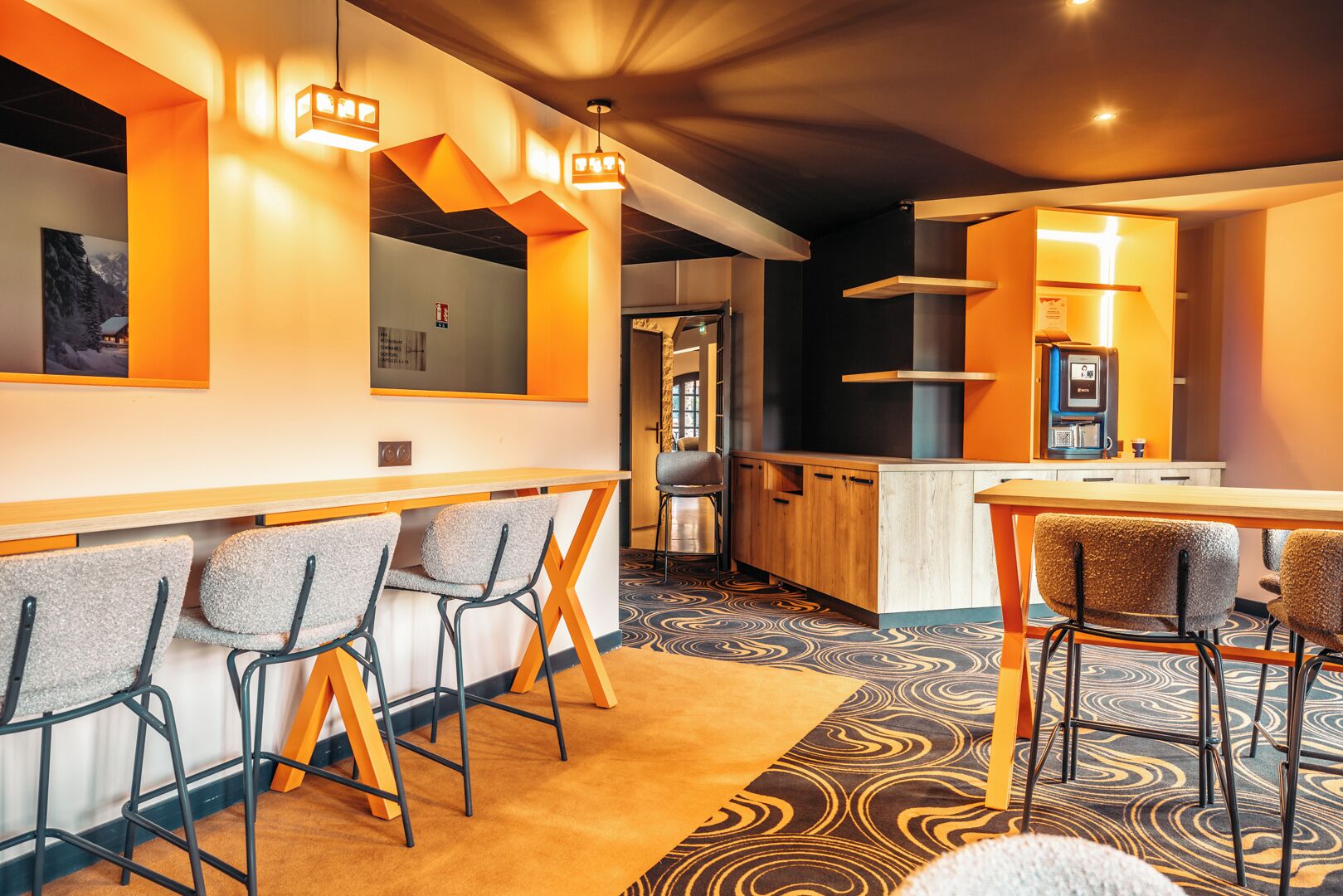 A modern bar area with seating, a kitchen, and a patterned carpet.