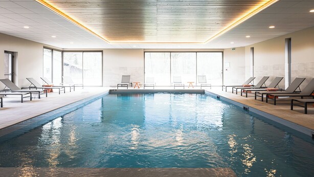 An indoor swimming pool with lounge chairs and a view of the outside. - Base Camp Lodge - Albertville (Albertville)