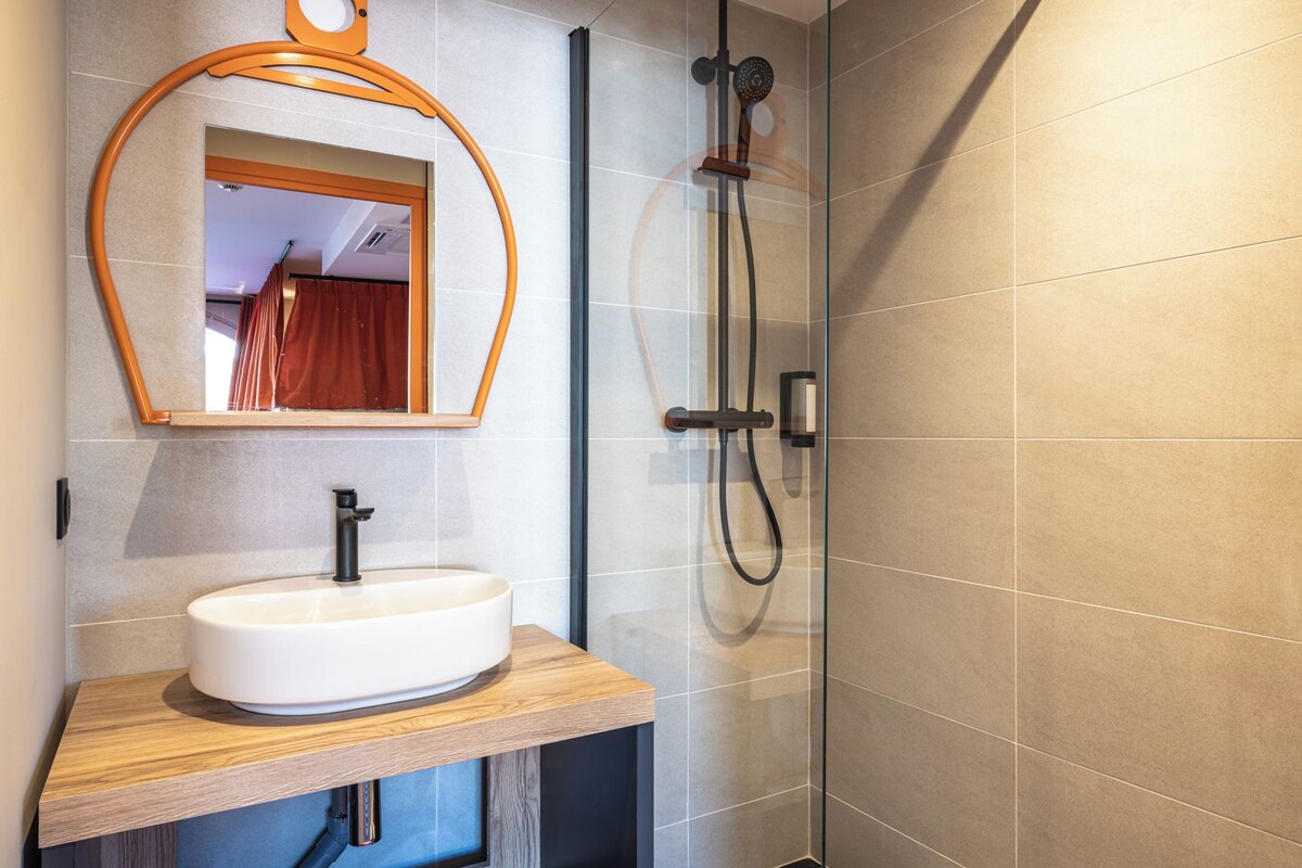 A modern bathroom with a wooden vanity, a round mirror, and a glass shower enclosure.