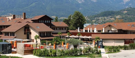 A hotel with multiple buildings, outdoor seating areas, and a mountain backdrop.