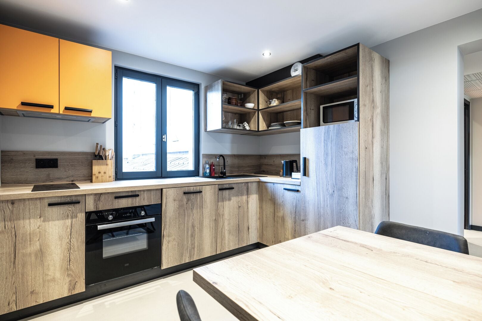 Een moderne keuken met houten kastjes, een inbouwoven en een raam.