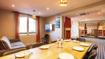 A hotel room with a dining table set for four, a sofa, a TV, and a mountain-themed wall.
