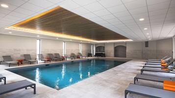 A modern indoor swimming pool with lounge chairs and a wooden ceiling.