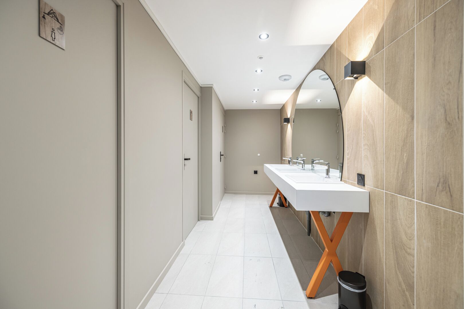 Une salle de bain moderne, de forme longue et étroite, dotée d’un meuble-lavabo à deux vasques et d’un grand miroir.