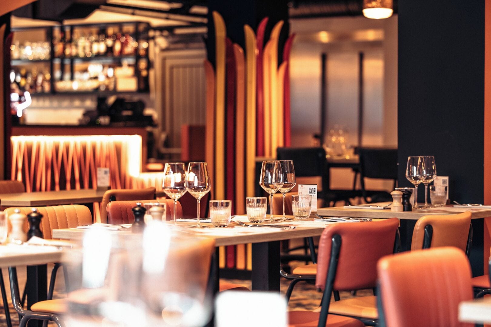 Een restaurant met gedekte tafels, glazen en een bar op de achtergrond.