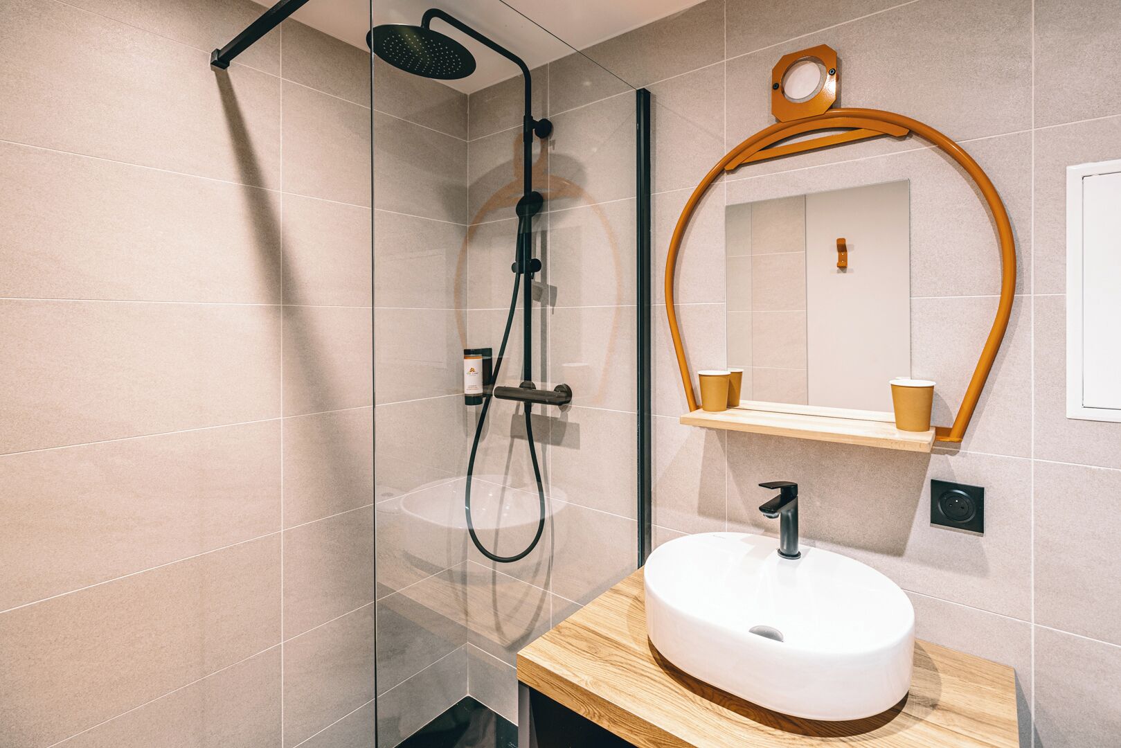 A modern bathroom with a glass-enclosed shower, a wooden vanity with a sink, and a mirror with a wooden frame.