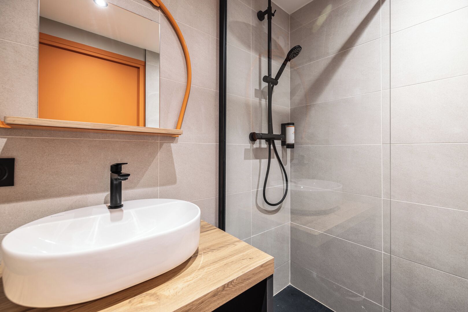 A modern bathroom with a white sink, a wooden countertop, and a shower with a handheld showerhead.