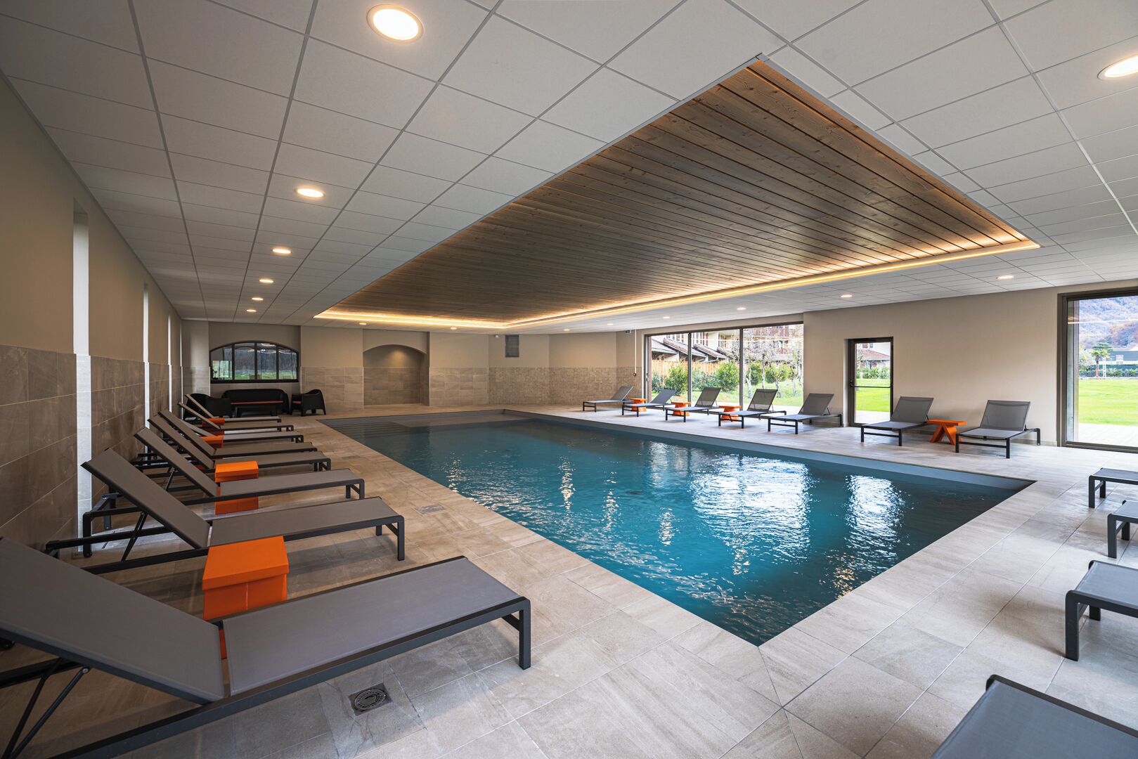 Piscina interior moderna con sillas de descanso y vistas al exterior.