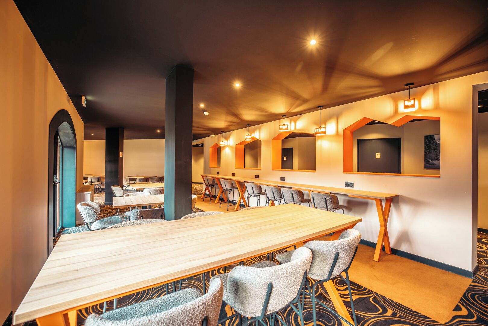 A conference room with a long table and multiple chairs, a high ceiling with recessed lighting, and a patterned carpet.